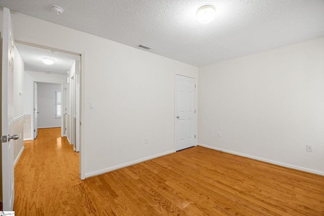 empty room featuring light wood-style flooring, a textured ceiling, baseboards, and a smoke detector