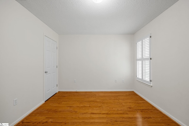 unfurnished room featuring light wood finished floors, a textured ceiling, and baseboards