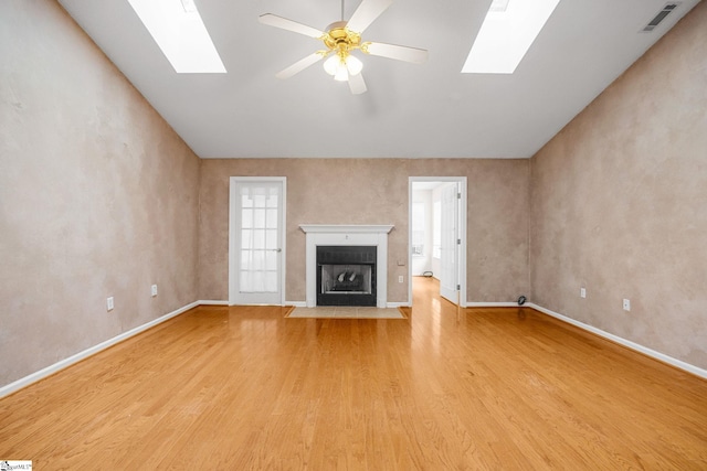 unfurnished living room with a skylight, light wood-type flooring, baseboards, a fireplace with flush hearth, and a ceiling fan