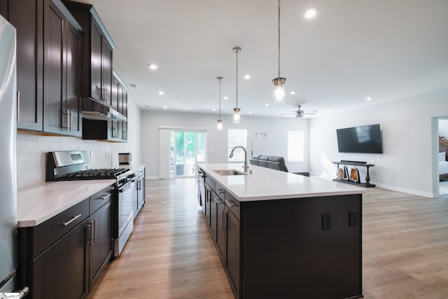 kitchen with stainless steel appliances, a sink, open floor plan, light wood finished floors, and recessed lighting