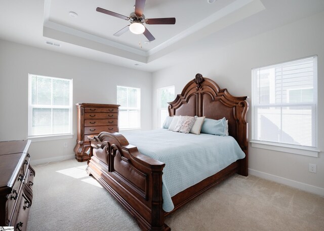 bedroom with a tray ceiling, light colored carpet, and multiple windows