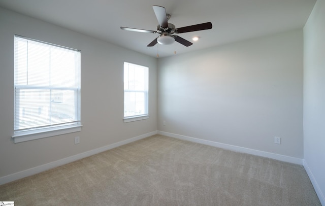 empty room featuring plenty of natural light, light colored carpet, baseboards, and a ceiling fan