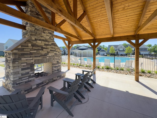 view of patio / terrace featuring an outdoor stone fireplace, fence, and a community pool
