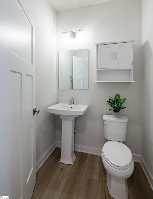 half bathroom featuring wood finished floors, baseboards, and toilet