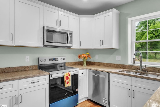 kitchen with stainless steel appliances, a sink, white cabinets, and light wood-style flooring