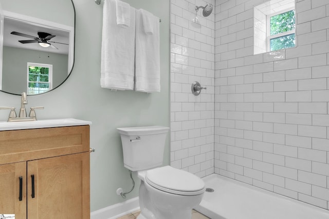 bathroom featuring toilet, ceiling fan, a tile shower, vanity, and baseboards