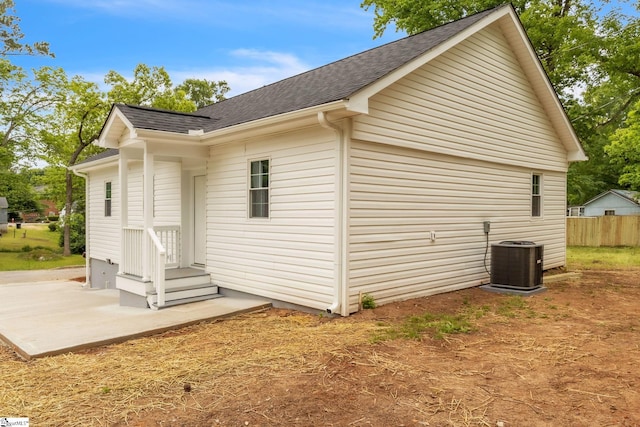 view of home's exterior featuring a shingled roof, central AC unit, a patio, entry steps, and fence
