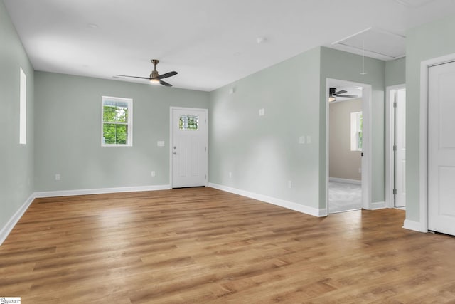 unfurnished living room with attic access, a ceiling fan, and baseboards