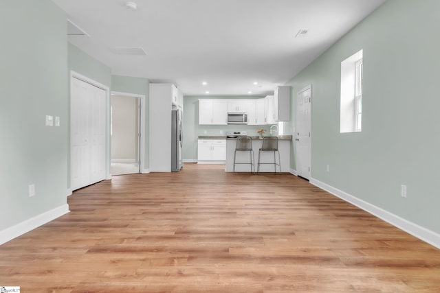 unfurnished living room with baseboards, light wood-type flooring, and recessed lighting