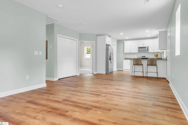unfurnished living room with attic access, light wood-type flooring, baseboards, and recessed lighting