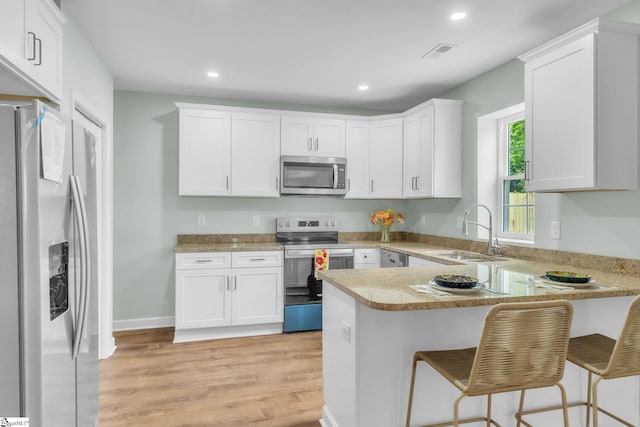 kitchen featuring stainless steel appliances, a sink, a peninsula, white cabinets, and light wood finished floors
