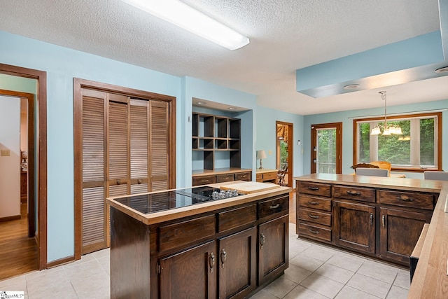 kitchen with black electric stovetop, a center island, dark brown cabinetry, light tile patterned flooring, and a textured ceiling