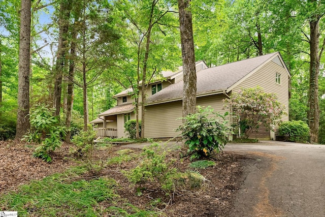 view of side of property featuring driveway and roof with shingles