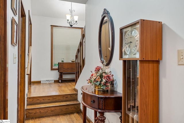 hall with wood finished floors, a chandelier, and stairway