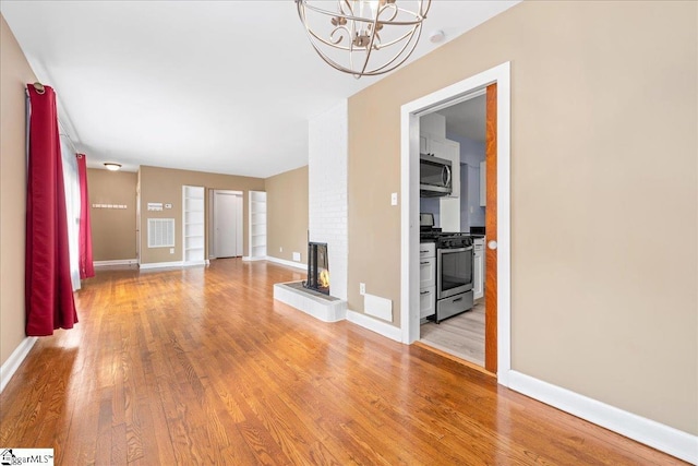 222 Woodview Ave, Spartanburg, SC 29306 - unfurnished living room featuring light wood-style flooring, a brick fireplace, a chandelier, and baseboards