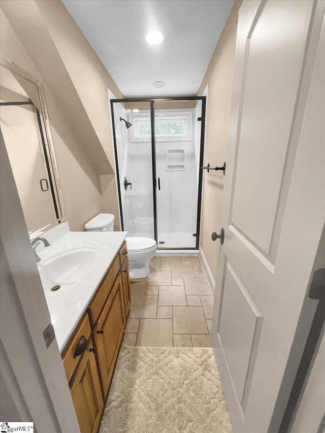 bathroom with a shower stall, toilet, stone tile flooring, vanity, and baseboards