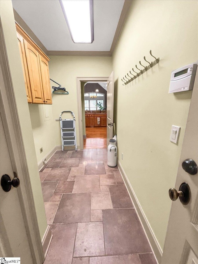laundry area featuring cabinet space, baseboards, stone finish flooring, and crown molding