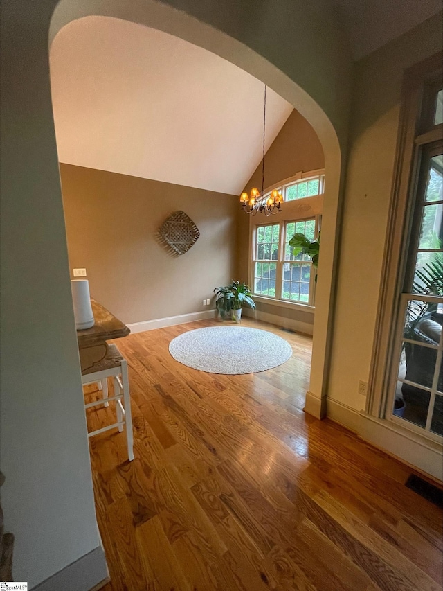 dining space with arched walkways, vaulted ceiling, wood finished floors, a chandelier, and baseboards