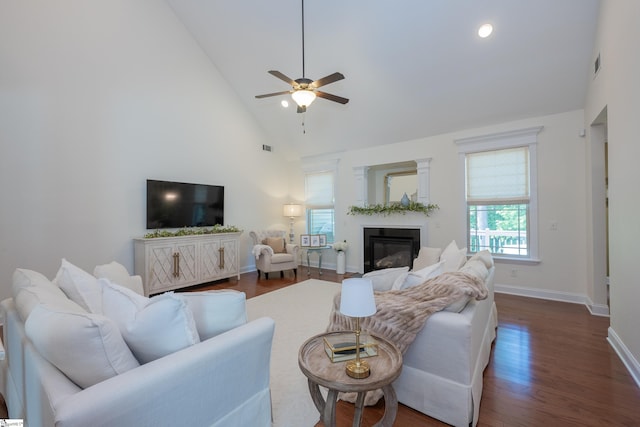 living area featuring dark wood-type flooring, a glass covered fireplace, baseboards, high vaulted ceiling, and ceiling fan