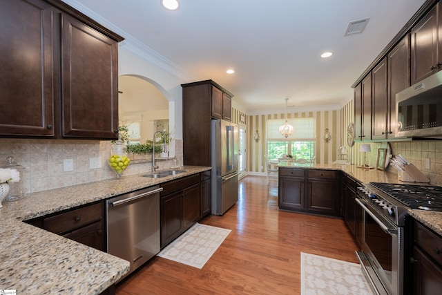 kitchen with premium appliances, a sink, dark brown cabinetry, ornamental molding, and a peninsula
