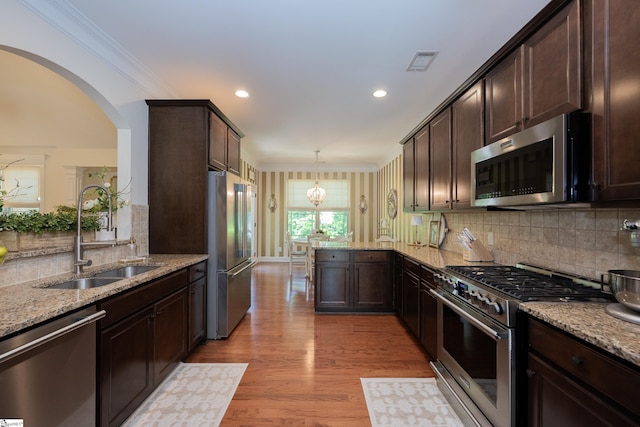 kitchen with high end appliances, a sink, a peninsula, dark brown cabinetry, and decorative backsplash