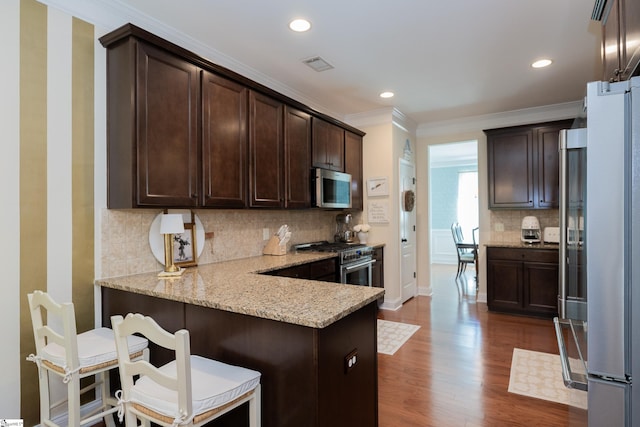 kitchen featuring stainless steel appliances, dark brown cabinets, crown molding, dark wood finished floors, and light stone countertops