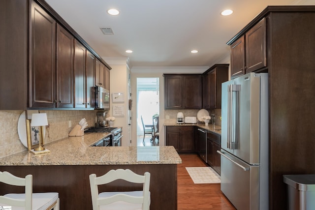 kitchen featuring high quality appliances, crown molding, dark brown cabinetry, dark wood-style flooring, and a peninsula