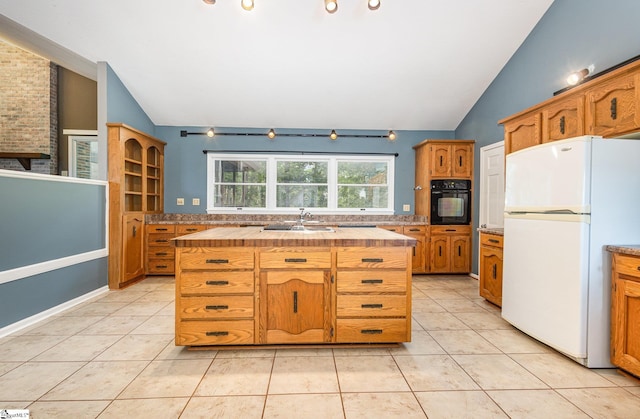 kitchen with freestanding refrigerator, black oven, lofted ceiling, butcher block countertops, and a sink
