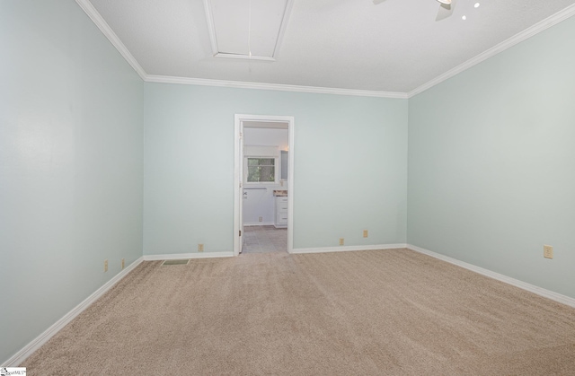 spare room with attic access, ornamental molding, light carpet, a ceiling fan, and baseboards