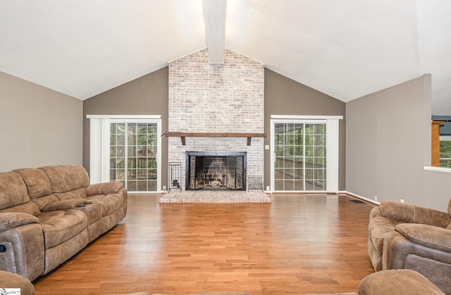 living room featuring high vaulted ceiling, light wood finished floors, beam ceiling, plenty of natural light, and a brick fireplace