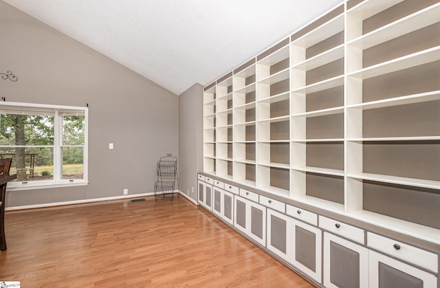 spare room with vaulted ceiling, light wood-type flooring, and baseboards