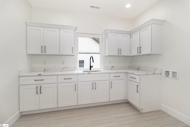 kitchen with a sink, baseboards, white cabinetry, light stone counters, and recessed lighting