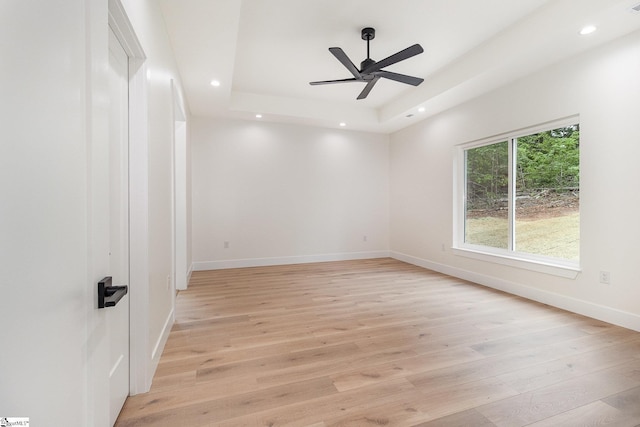 unfurnished room with a raised ceiling, light wood-style floors, recessed lighting, baseboards, and a ceiling fan