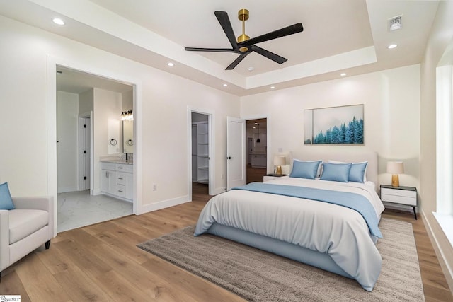 bedroom featuring a tray ceiling, light wood-style floors, a walk in closet, recessed lighting, and baseboards