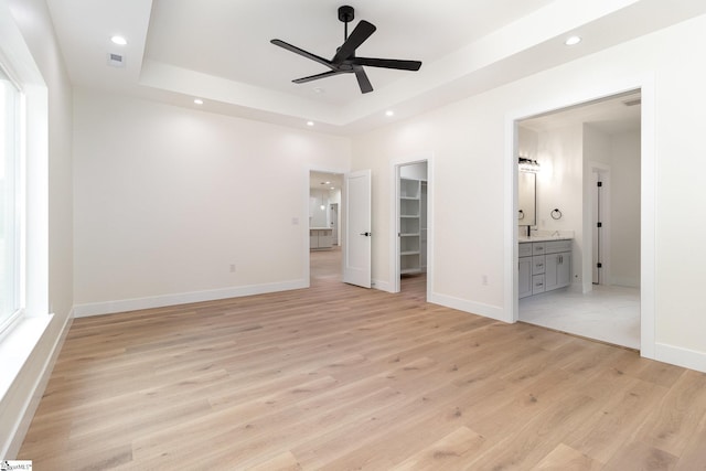 unfurnished bedroom featuring a spacious closet, light wood-style flooring, a tray ceiling, recessed lighting, and connected bathroom