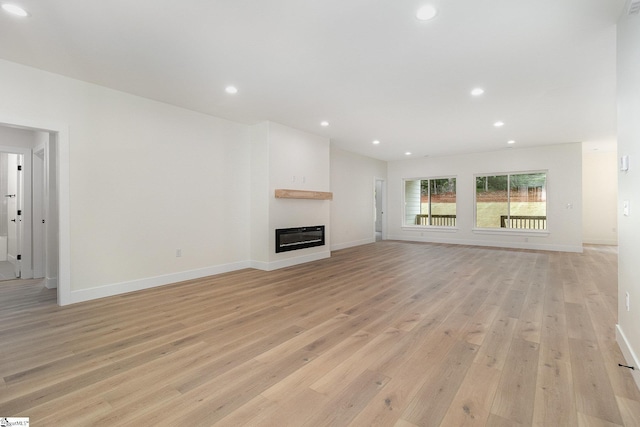 unfurnished living room with light wood-style floors, baseboards, a glass covered fireplace, and recessed lighting
