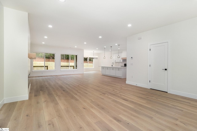 unfurnished living room with light wood-style flooring, recessed lighting, baseboards, and a sink