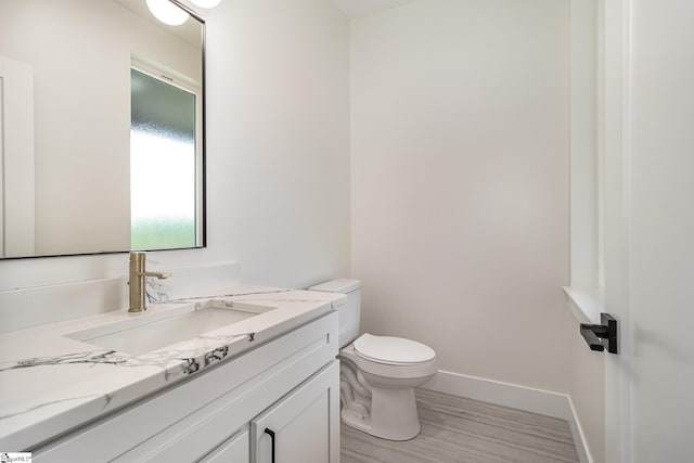half bath with wood finished floors, toilet, vanity, and baseboards
