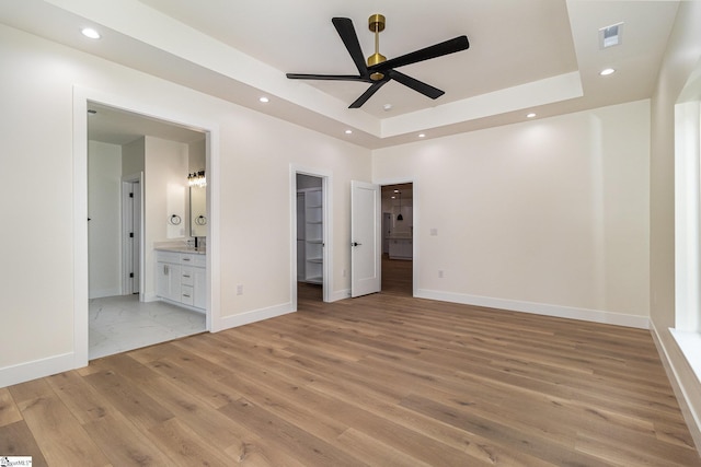 unfurnished bedroom with light wood-type flooring, a raised ceiling, a walk in closet, recessed lighting, and ensuite bathroom