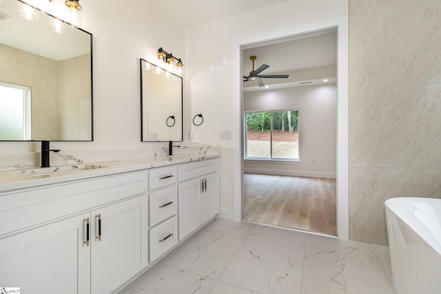 full bathroom with ceiling fan, a freestanding bath, double vanity, marble finish floors, and baseboards