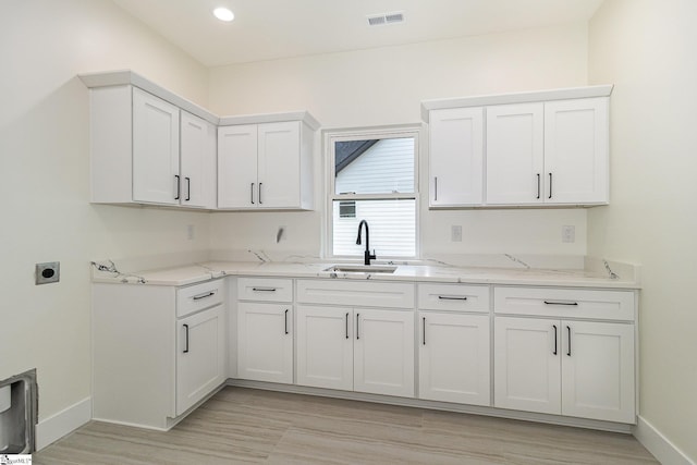 kitchen with a sink, white cabinetry, baseboards, light stone countertops, and light wood finished floors