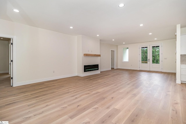unfurnished living room with light wood-type flooring, a glass covered fireplace, recessed lighting, and baseboards