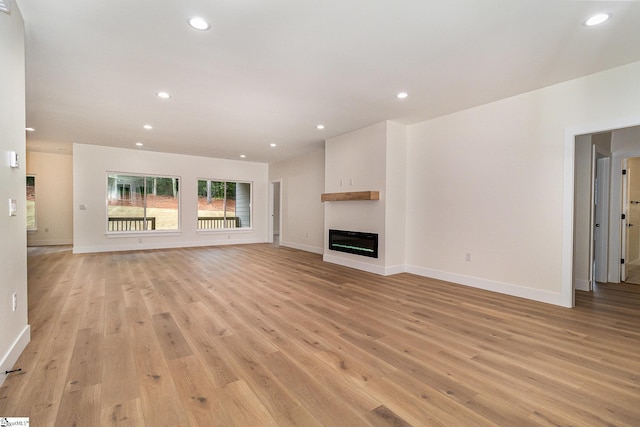 unfurnished living room featuring light wood finished floors, recessed lighting, baseboards, and a glass covered fireplace