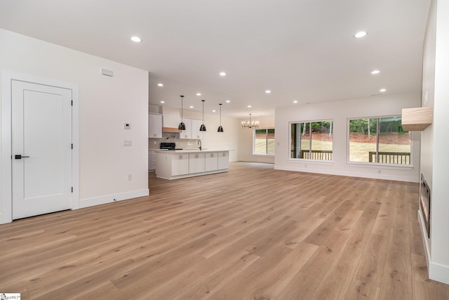 unfurnished living room with plenty of natural light, light wood-type flooring, a chandelier, and recessed lighting