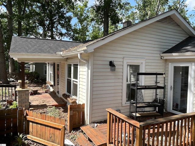 view of side of property with roof with shingles, a deck, a chimney, and fence