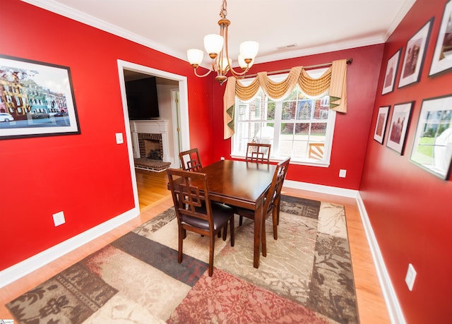 dining room featuring a chandelier, wood finished floors, a brick fireplace, baseboards, and ornamental molding