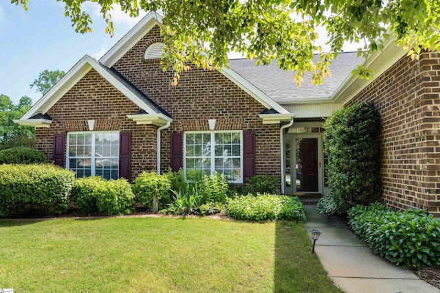view of front of home featuring brick siding, a front yard, and a shingled roof
