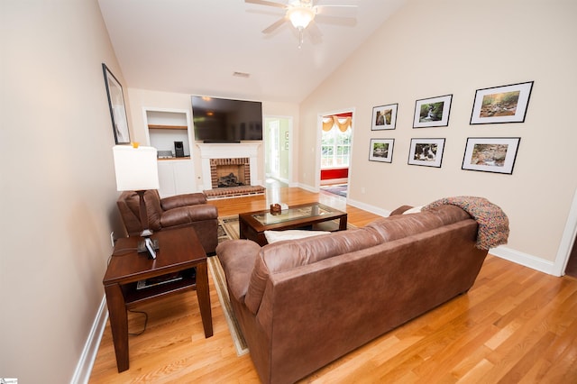living area with a ceiling fan, light wood-type flooring, baseboards, a brick fireplace, and high vaulted ceiling