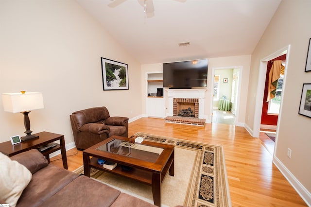 living room with lofted ceiling, light wood-style flooring, a ceiling fan, baseboards, and a brick fireplace