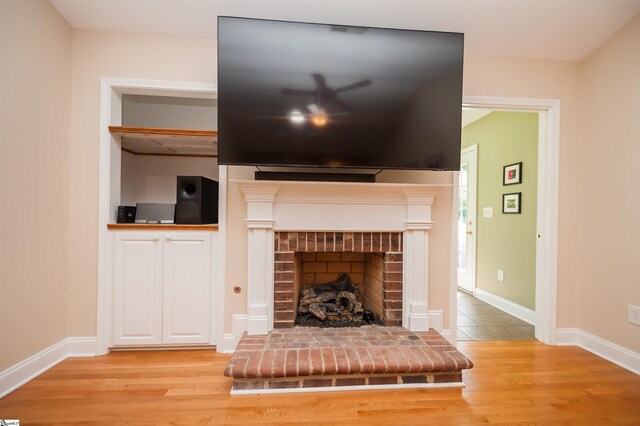 living area with light wood finished floors, a brick fireplace, and baseboards